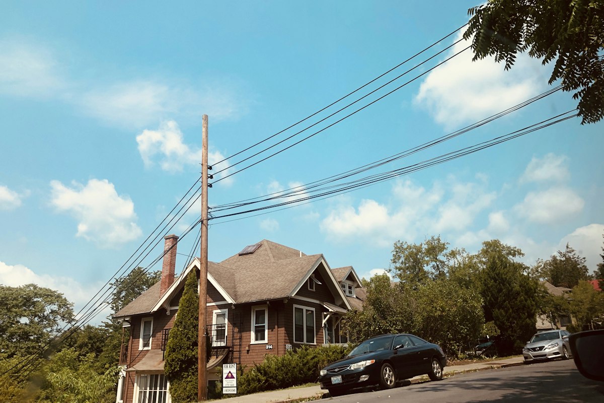A street photo of a brick house with a car and power lines